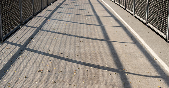 the metal railing of a pedestrian bridge casting shadows on the asphalt