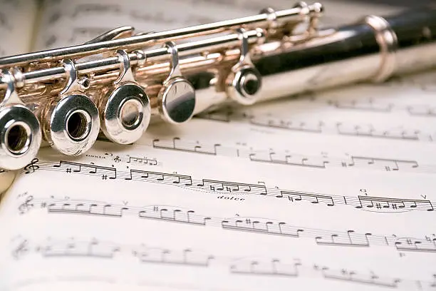 A used flute rests across an open musical score. Only one line of music is in focus.