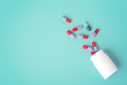 Spilled pills with white medicine bottle on green background with copy space, top view