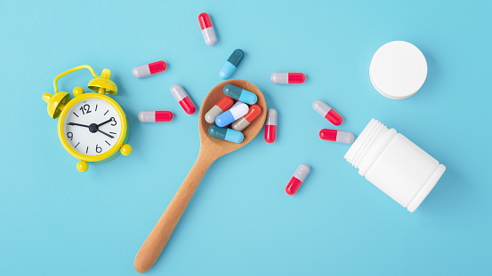 Medicine time concept with capsule pills on spoon and alarm clock on blue background