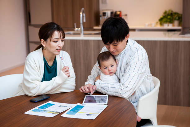 赤ちゃんを連れたアジアの若いカップルは、自宅で一緒にファイナンシャルプランニングについて話し合っています。 - 貯金 ストックフォトと画像