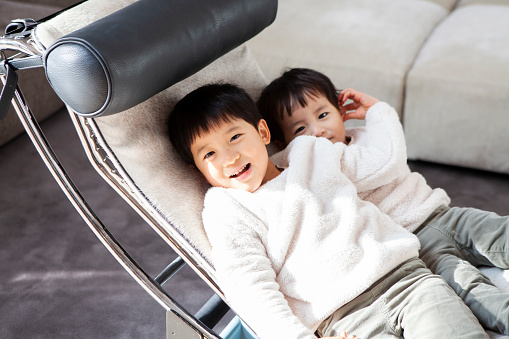 Young brothers lying down on a modern rocking chair.
Good friends are playing happily.