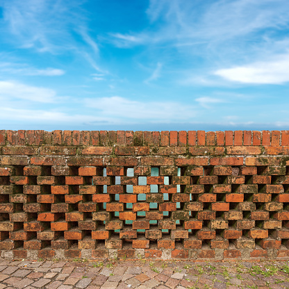 Close-up of a railing of a bridge (parapet) made of old bricks against a blurred blue sky with clouds. Veneto, Italy, Europe.