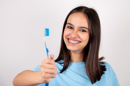Portrait of a happy teen girl with braces holding a toothbrush smiling. Isolated on white