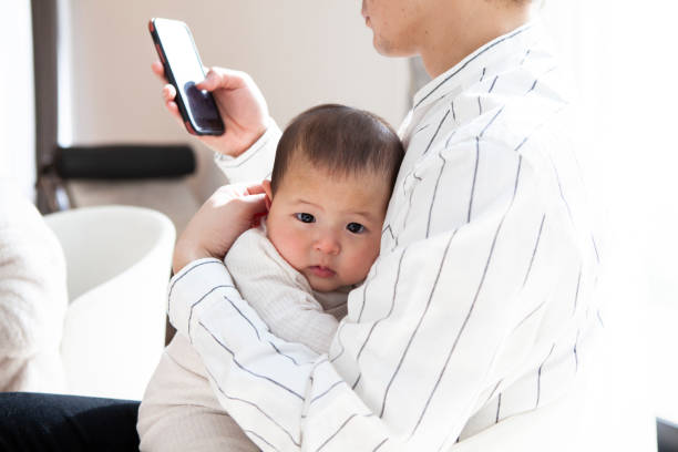 istock Young dad sitting on the sofa and holding his baby while using smartphone. 1397006630