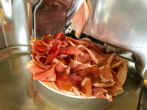 Someone cutting slices of raw ham with a stainless steel meat slicer.