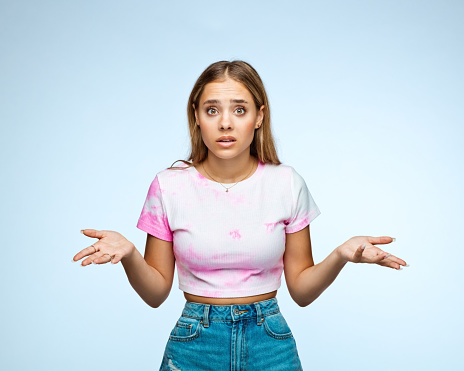 Portrait of teenage girl with surprised facial expression gesturing against white background.