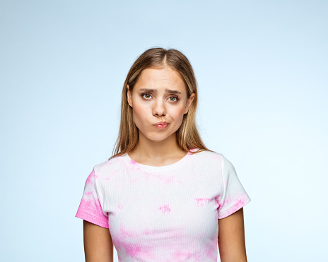 Portrait of blond teenage girl in tie dye t-shirt making face against blue background
