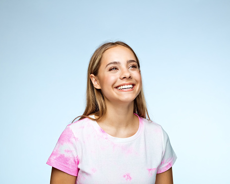 Close up portrait of beautiful little girl with blonde long hair and big blue eyes looking at camera with relaxed expression. Nature background.