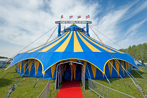 Circus Big Top and entrance lighting, A505 near Royston, Cambridge, England. Traditional colorful tents and bright lights typify the old characteristics of circus life, which no longer features wild animals but still provide hours of fun for families and children