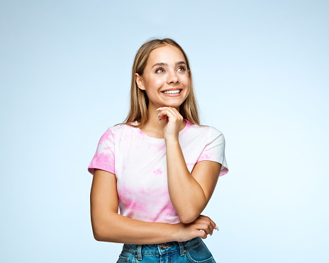 Happy teenage girl with hand on chin looking up against blue background