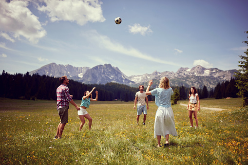 Group of friends having fun playing with ball on green meadow. Enjoying time together in nature. Fun, togetherness, lifestyle, nature concept.