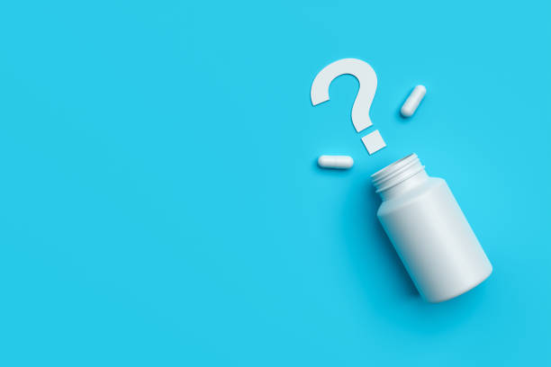 Plastic medical container and white capsule pills with question mark on blue background copy space top view. stock photo
