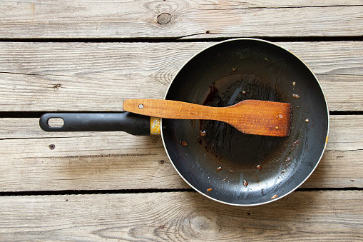 A frying pan and a wooden spatula with leftover fry food on a wooden table at home in the kitchen, dirty dishes, an old frying pan