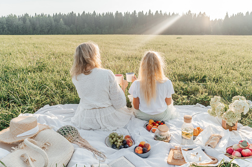 Mother and daughter on picnic in field. Fruits and tea on a blanket. White cloth, sunny day.