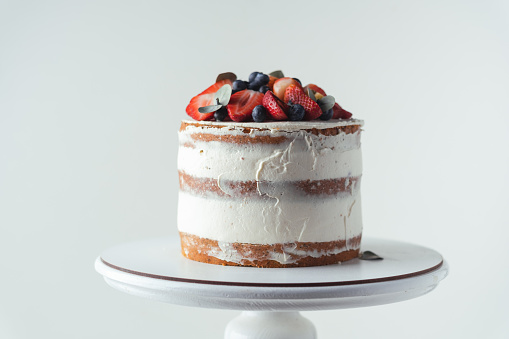 summer vanilla sponge cake with cream cheese filling decorated with strawberries and blueberries on top on a white background. White cake stand