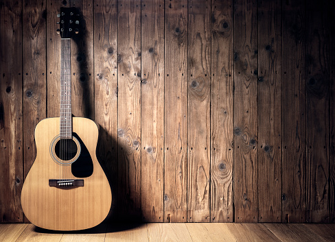 Acoustic guitar resting against a blank wooden plank grunge background with copy space