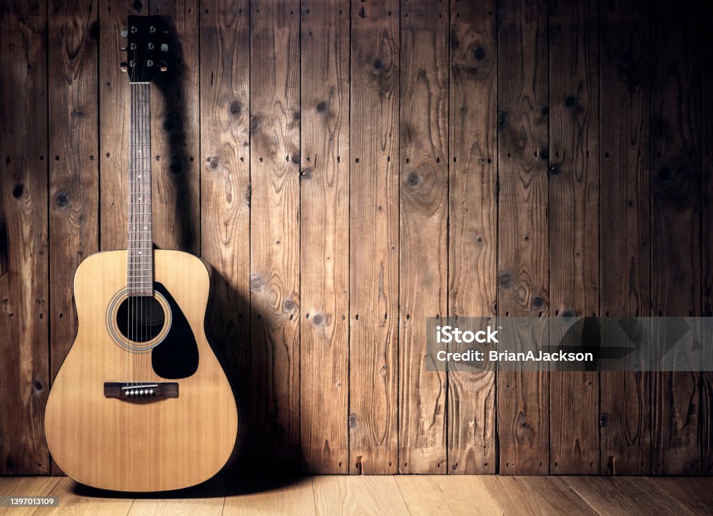 Acoustic guitar against blank wooden plank panel grunge background with copy space Acoustic guitar resting against a blank wooden plank grunge background with copy space Guitar Stock Photo