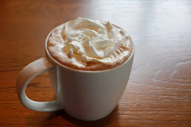 Photo of Closeup hot mocha fresh coffee in a white cup with whipping cream on wooden table background. Drink concept.