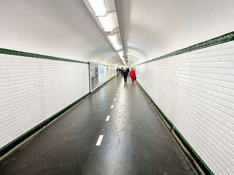 Paris Métro with a long connection tunnel with advertising at the walls. The image shows atunnel connecting two different Metro Lines with several people.