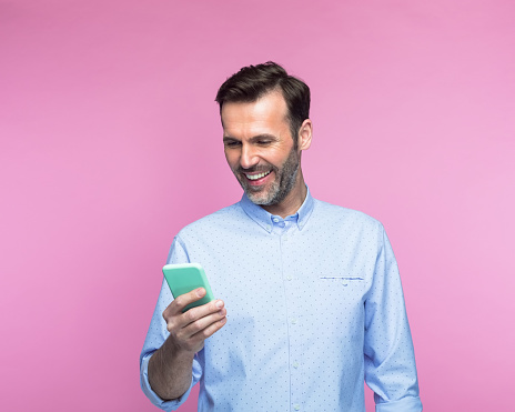 Happy mid adult man using smart phone against pink background
