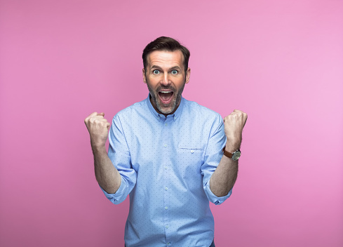 Portrait of happy man screaming with clenched fists against pink background