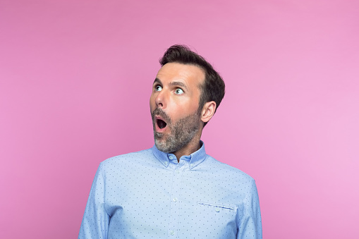 Shocked mid adult man looking up against pink background