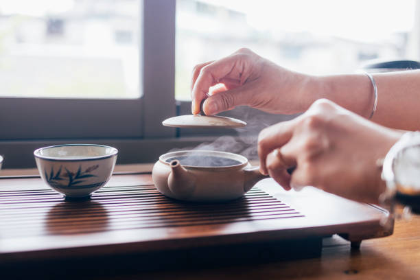 Close up shot of an anonymous woman holding a lid of a teapot ready to pour some tea in the cup.