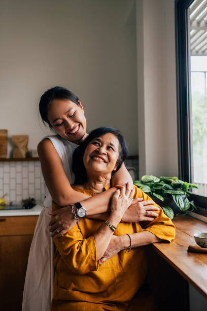 porträt einer asiatischen zweierfamilie, mutter und tochter, die in einer küche sitzt, tochter, die ihre mutter mit viel liebe und hingabe umarmt. - thai culture fotos stock-fotos und bilder