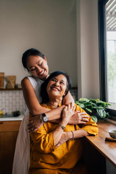 портрет азиатской семьи из двух человек, матери и дочери, сидящей на кухне, дочери, обнимающей маму с большой любовью и преданностью. - family adult portrait parent стоковые фото и изображения