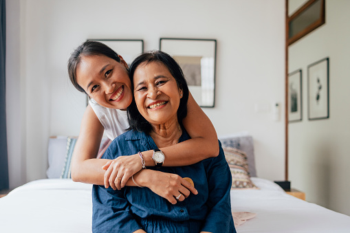 Portrait of Asian family of two, mother and her daughter looking at the camera, smiling, A daughter is hugging her mother from behind.