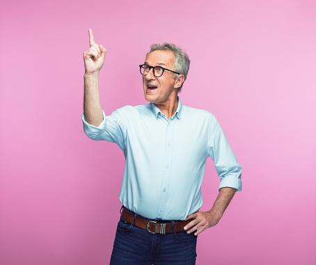 Excited senior man gesturing while looking up against pink background