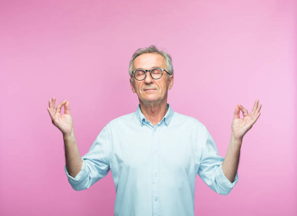 Relaxed elderly man meditating with eyes closed Relaxed retired elderly man meditating with eyes closed against pink background serene people stock pictures, royalty-free photos & images