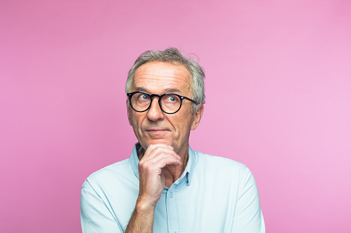 Thoughtful senior man with hand on chin looking away against pink background