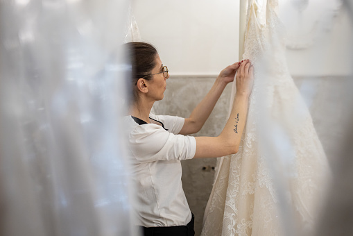 Caucasian female saleswoman at the bridal shop, arranging wedding dresses