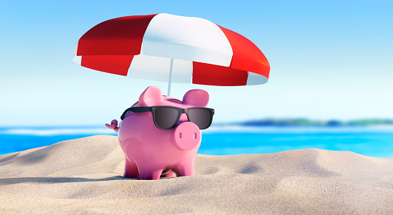 Piggy bank with sunglasses and umbrella at empty beach background