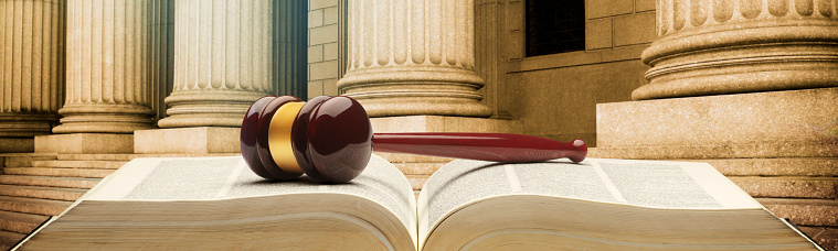 A gavel rests on an open law book in front of a row of columns.