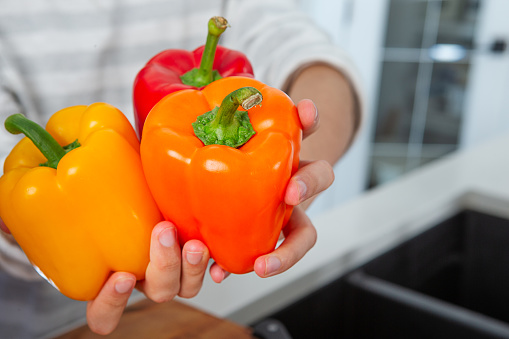 Male hand holding mixed colour of peppers in kitchen.