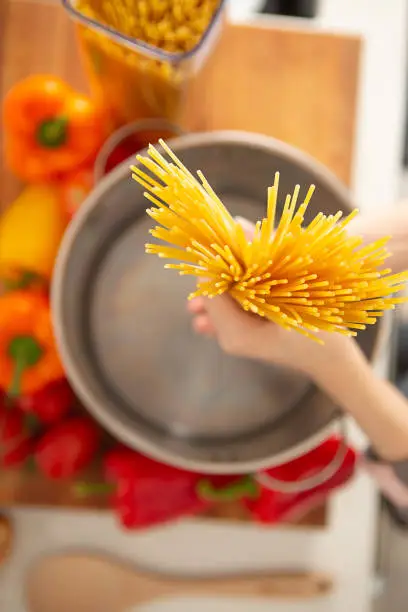 Above view of hand holding a handful of raw pasta noodle in pot in kitchen