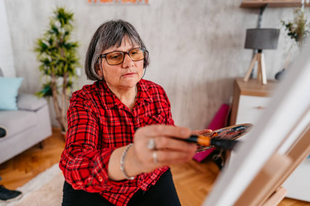 Senior Female Artist Painting At Home Senior woman artist painting in her living room at home. painted image paintings oil paint senior women stock pictures, royalty-free photos & images