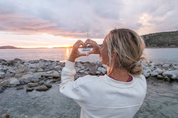 a una mujer joven le encanta la puesta de sol y hace un marco de dedos en forma de corazón sobre el sol - blond hair overcast sun sky fotografías e imágenes de stock