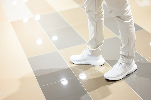 Male legs wearing casual white trousers and shoes walking on glossy floor in shopping mall. Fashion footwear concept