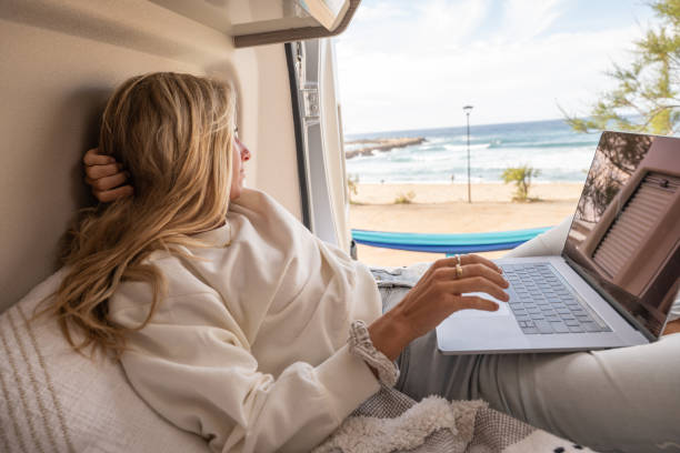 woman working online from her campervan - on beach laptop working imagens e fotografias de stock