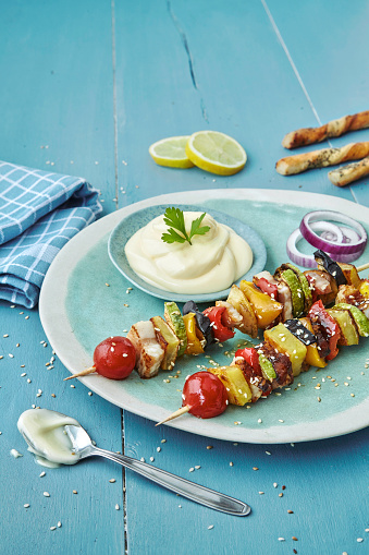Modern meat and vegetable skewers in a beautiful blue environment. Skewers can be made from pork meat, chicken or beef meat, or from vegetables if you wish to make a vegetarian skewers. Usually they are served with different style veggies and baked potatoes, with chopped garlic and onion, along with mayo sauce. They can be served on plate, tortilla or pita bread, with fresh lemon or cilantro, with salt and persil. As garnish you can add salad or bread sticks. Colorful. Fresh and Tasty. Vertical. South America delicates. European food. Asian food. Indian food. Mexican food. Balkan food. Beautiful.