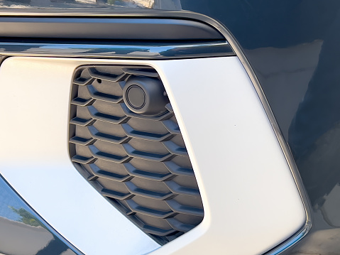 Selective focus parking sensor at front car bumper on light blurred background
