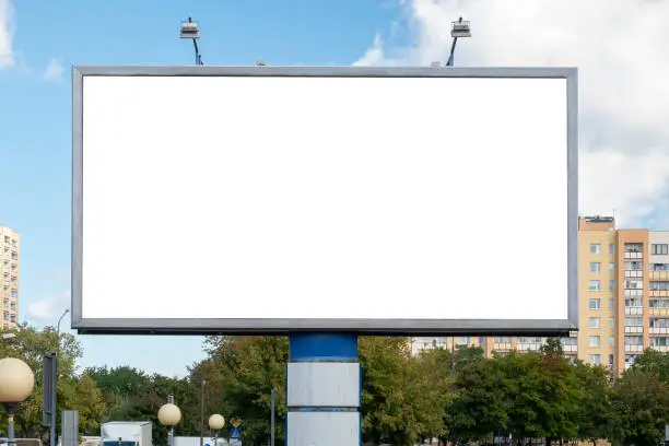 Photo of Blank white advertising billboard near residential buildings in the city on a sunny summer day.