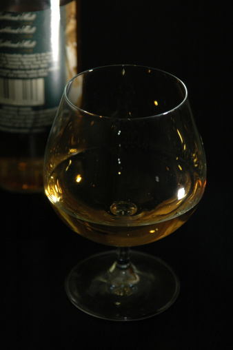 Scotch in a snifter glass. Bottle is visible in the behind, black background.