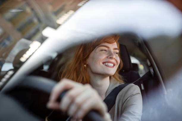 日没時に新しい車を運転する美しい若い女性。車に乗った女性。嬉しそうなポジティブな表情をした愉快そうな女性のクローズアップ肖像画、車を運転するカジュアルウェアの女性 - driving ストックフォトと画像