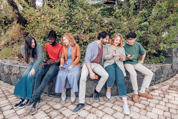 istock group of multiethnic friends students sitting on a low wall talking and looking at mobile phones 1397040068
