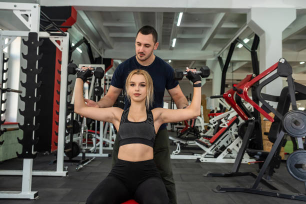 istock personal trainer with slim woman client doing bicep curls working out in gym 1397040082
